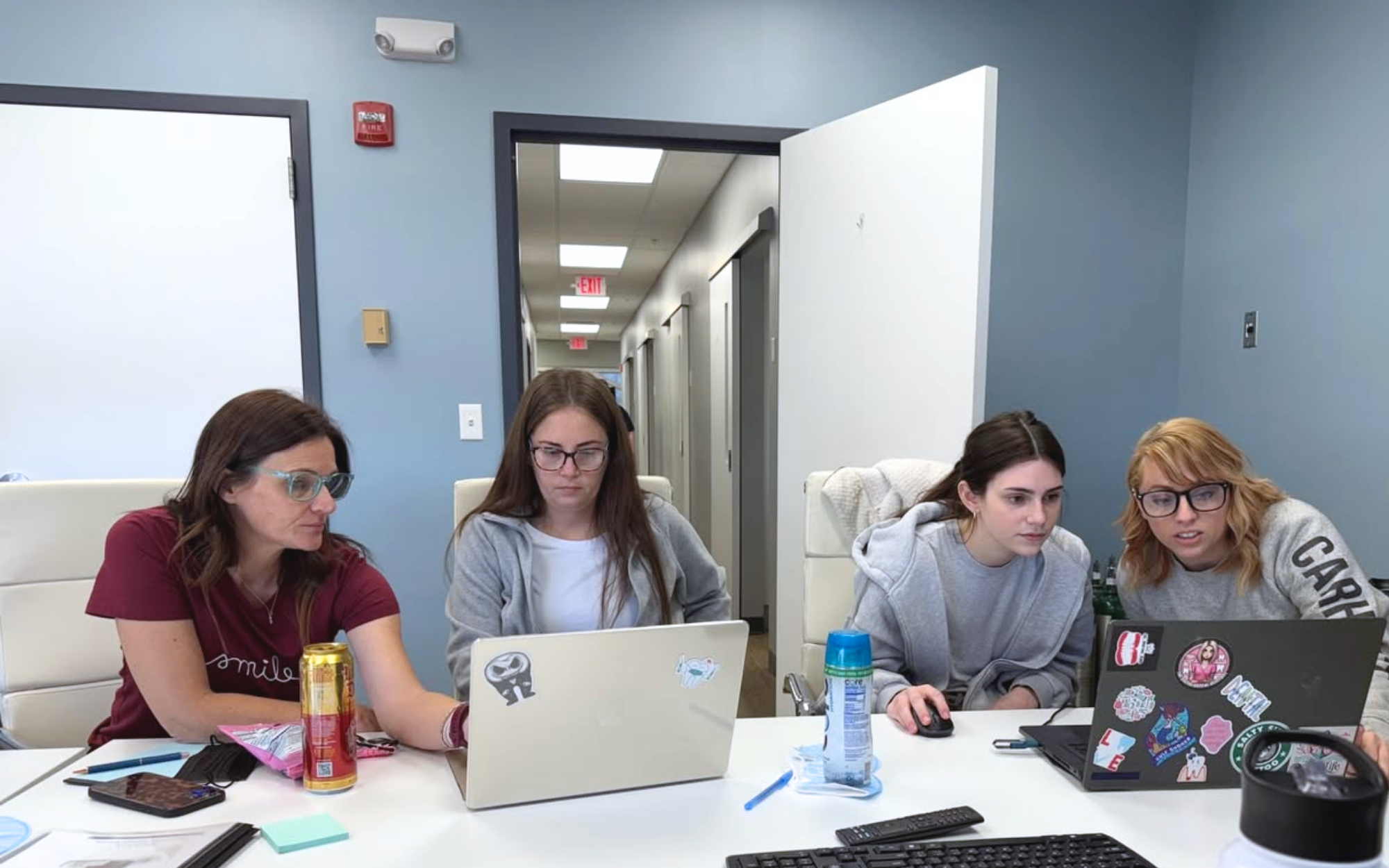Four women working on laptops together at table in office