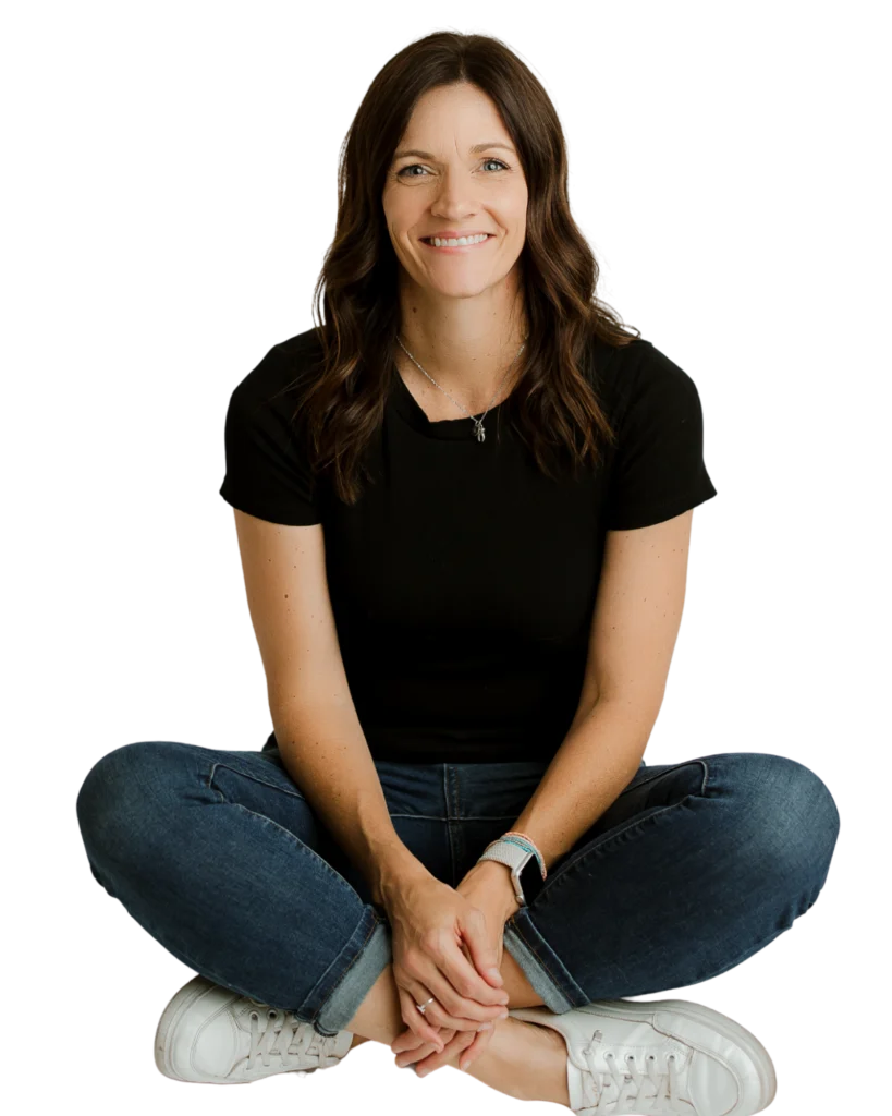 Smiling woman sitting cross-legged wearing black shirt, jeans, and white sneakers