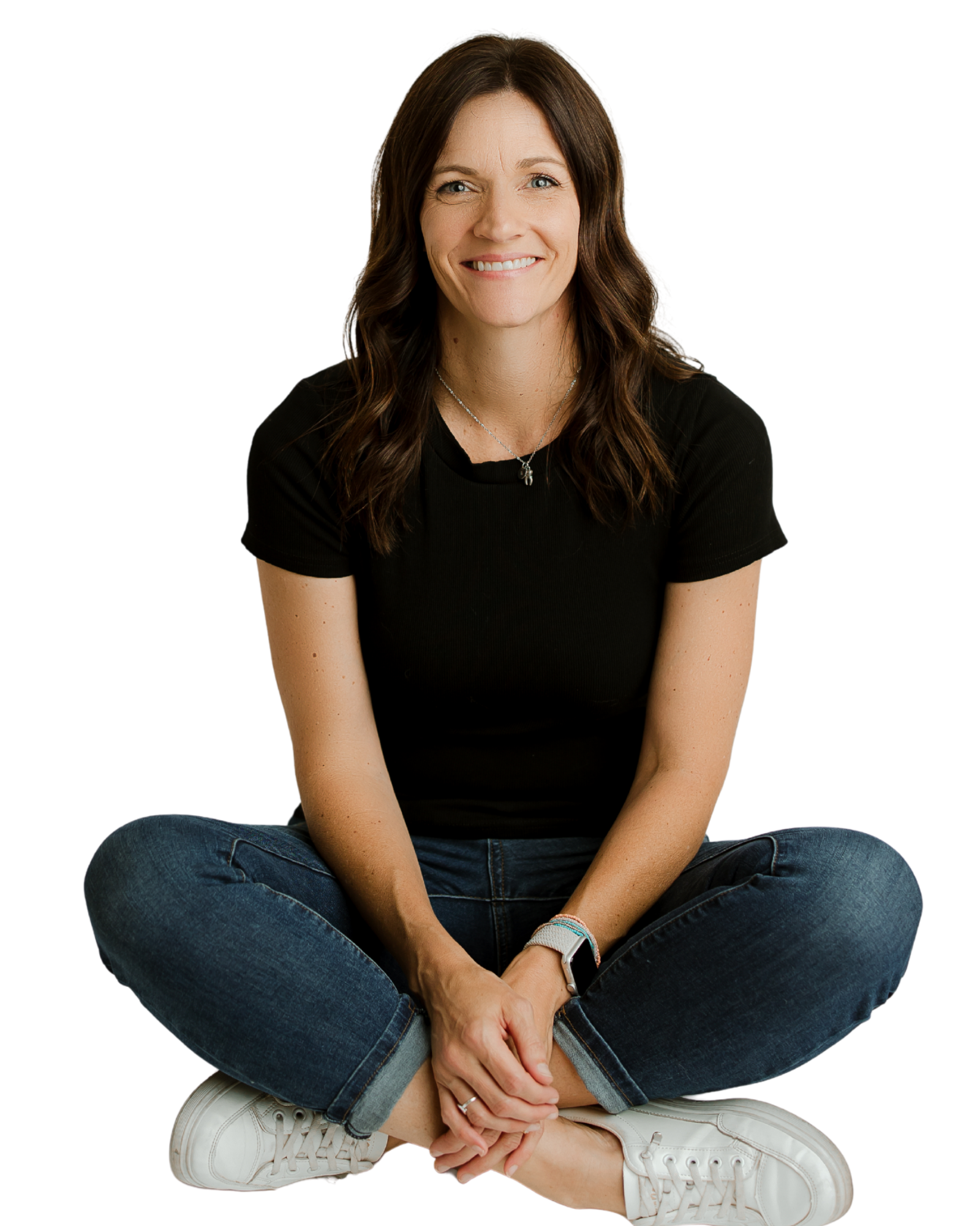 Smiling woman sitting cross-legged wearing black shirt, jeans, and white sneakers