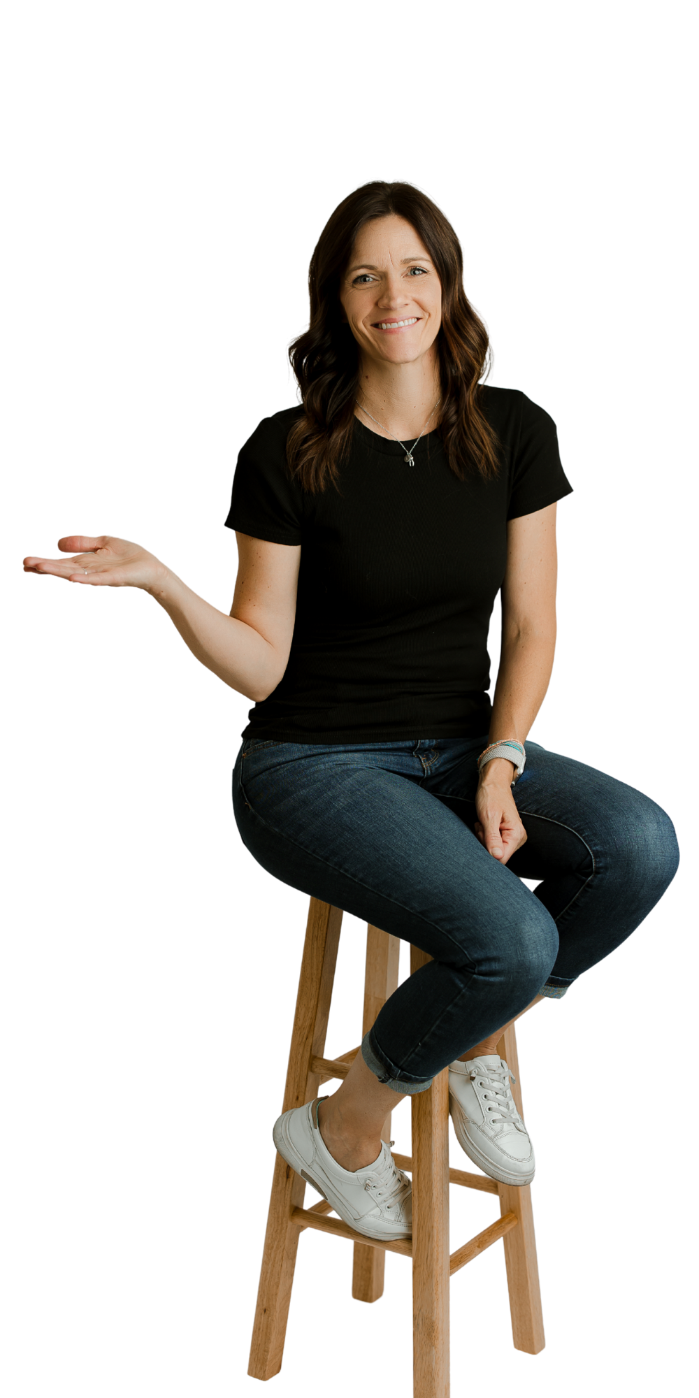 Woman sitting on stool smiling and gesturing with open hand